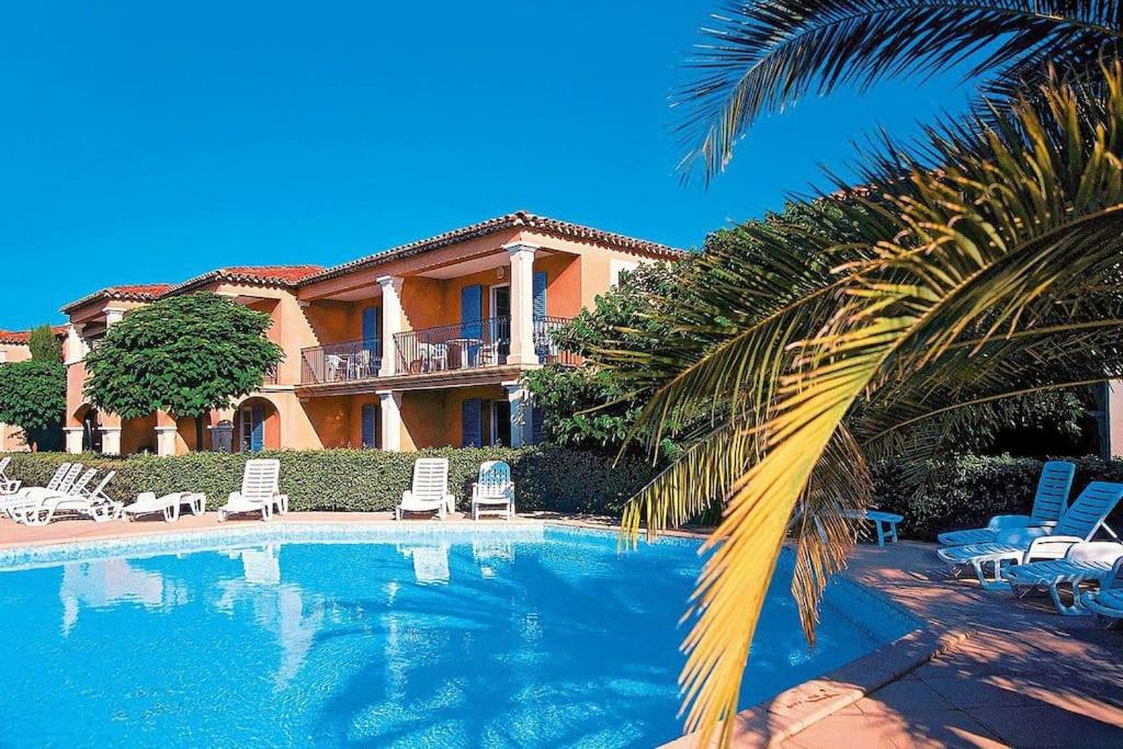 una casa con una piscina con sillas y una palmera en Appartement La Palmeraie Odalys Prestige Grimaud en Grimaud
