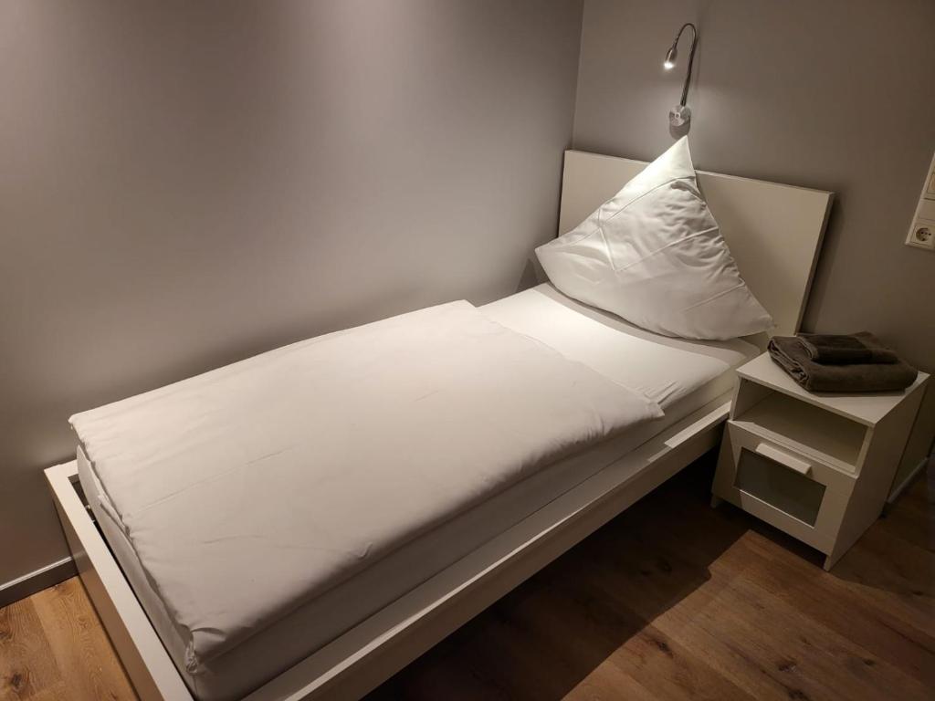 uma pequena cama com lençóis brancos e uma mesa de cabeceira em "Anderer´s" Gasthaus & Hotel Hohne em Hohne