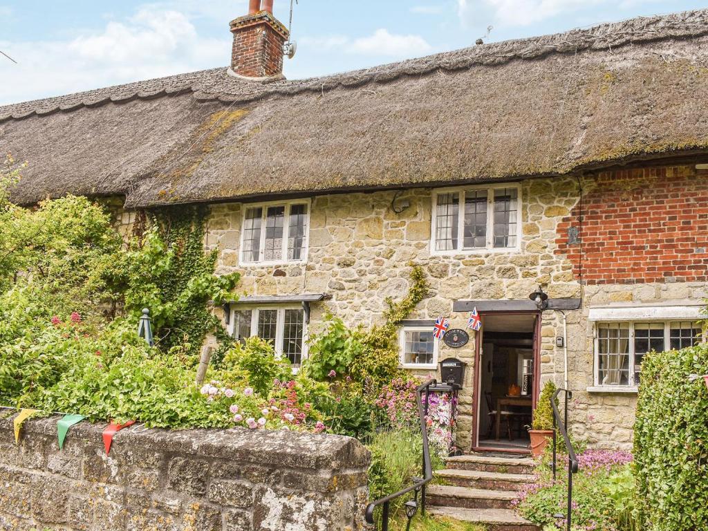 an old stone house with a thatched roof at Plum Tree Cottage in Fontmell Magna