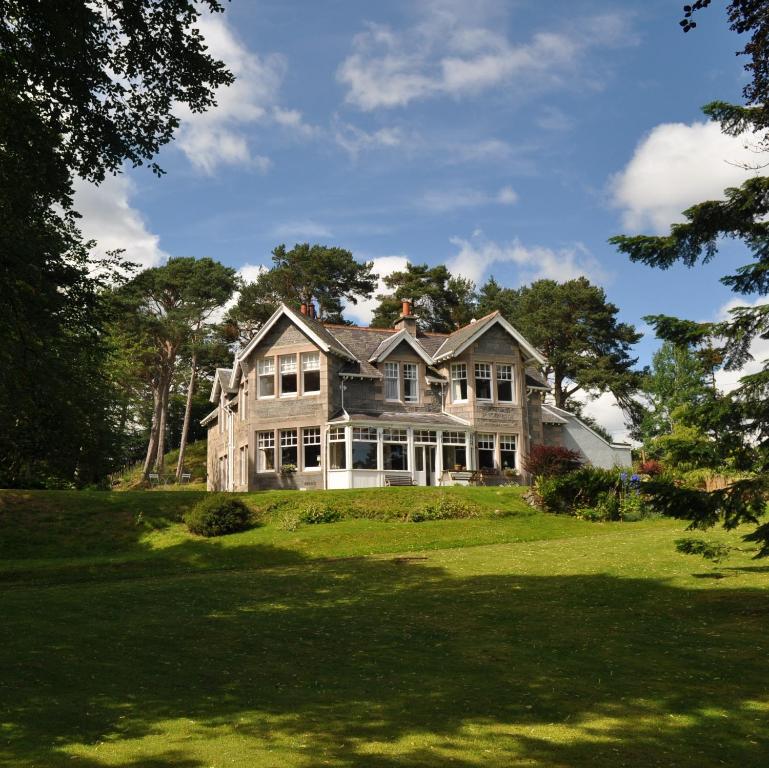 una grande casa su un campo verde con alberi di Coig na Shee Guest House a Newtonmore