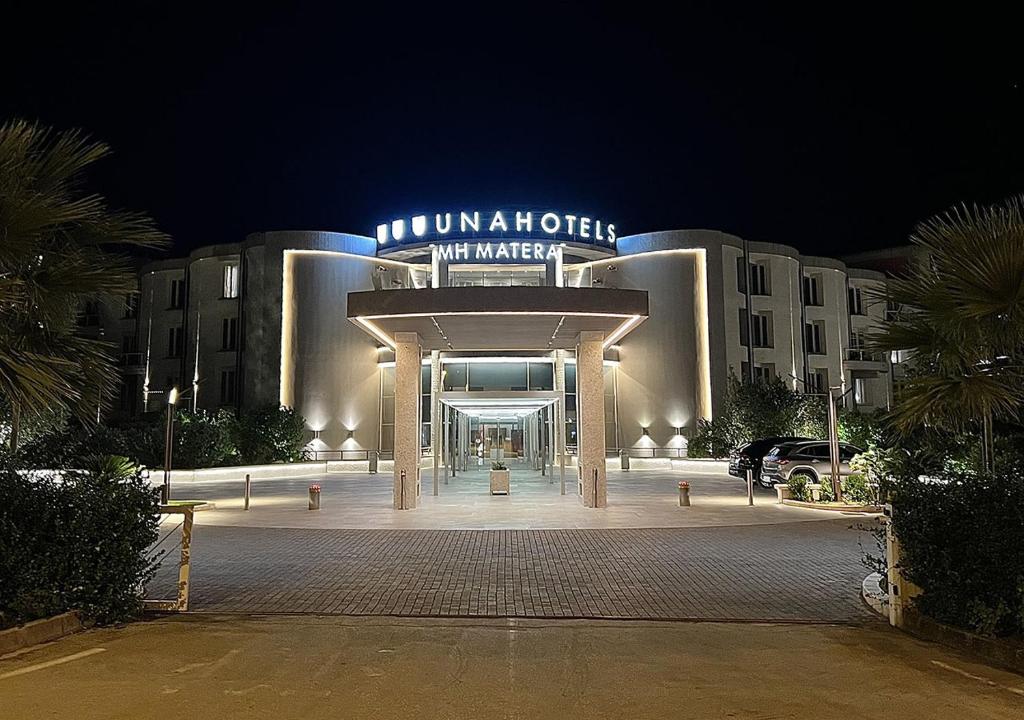 a large building with a sign on it at night at UNAHOTELS MH Matera in Matera