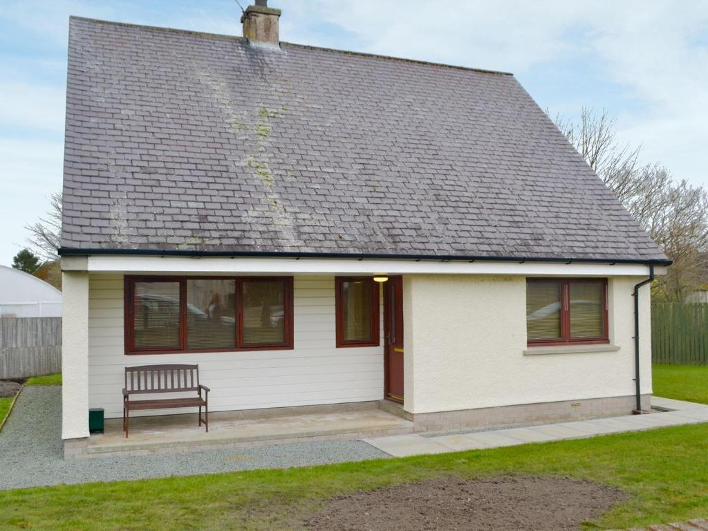 una pequeña casa blanca con un banco en un patio en Cluaran Cottage en Tain