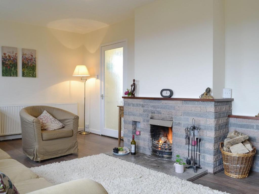 a living room with a brick fireplace and a chair at Beuchan Bungalow in Closeburn