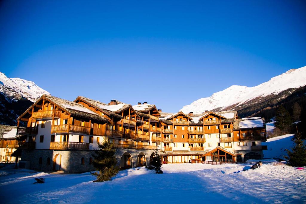 un grand bâtiment dans la neige avec des montagnes enneigées dans l'établissement Les Alpages De Val Cenis by Resid&co, à Lanslebourg-Mont-Cenis