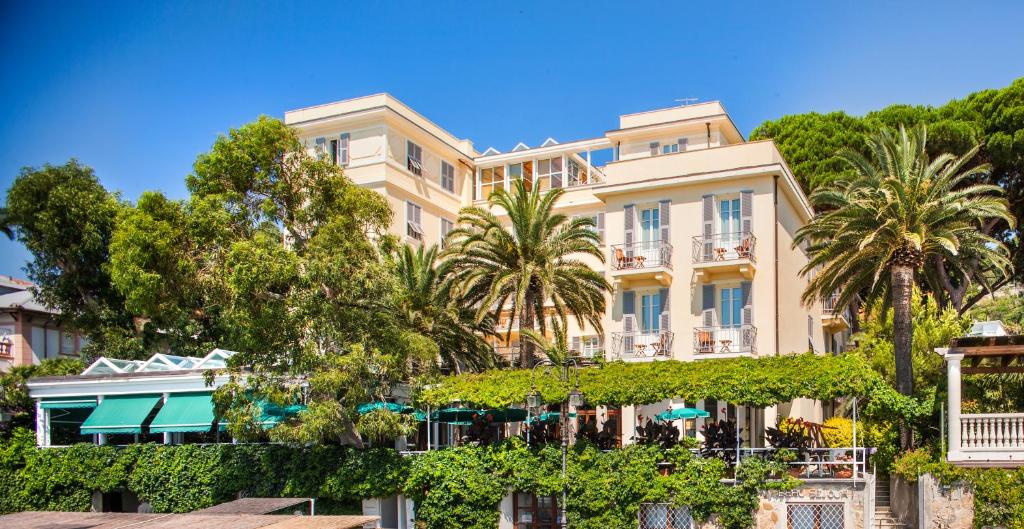 un grand bâtiment avec des arbres devant lui dans l'établissement Hotel Beau Sejour, à Alassio