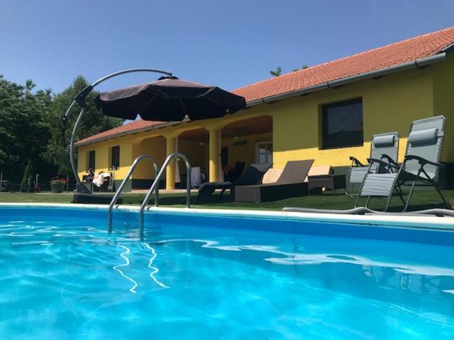 Nagykőrös的住宿－Sunshine Tanya，一个带遮阳伞和椅子的游泳池以及一座房子