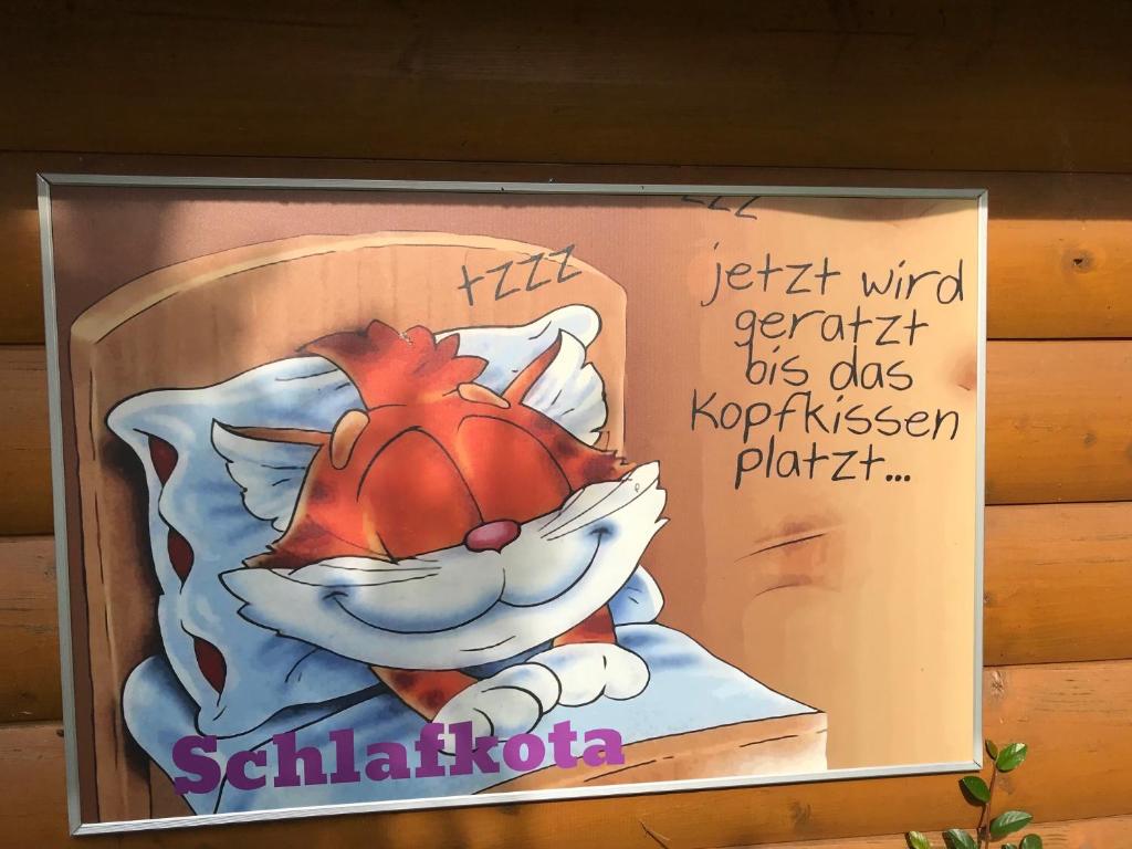 Schlafkota vom Friesenhof Wieratal : لوحة عليها قطة كرتونية ملقاة على السرير