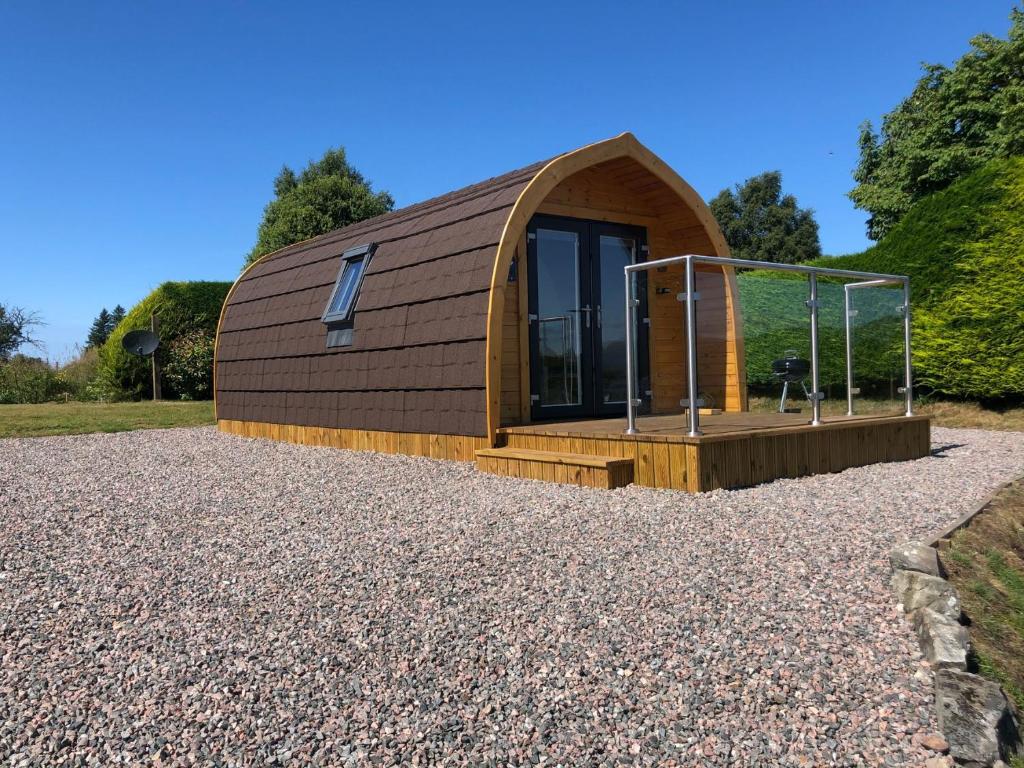 a small cabin with a wooden roof on a gravel yard at Burnbank Glamping Pod in Acharacle