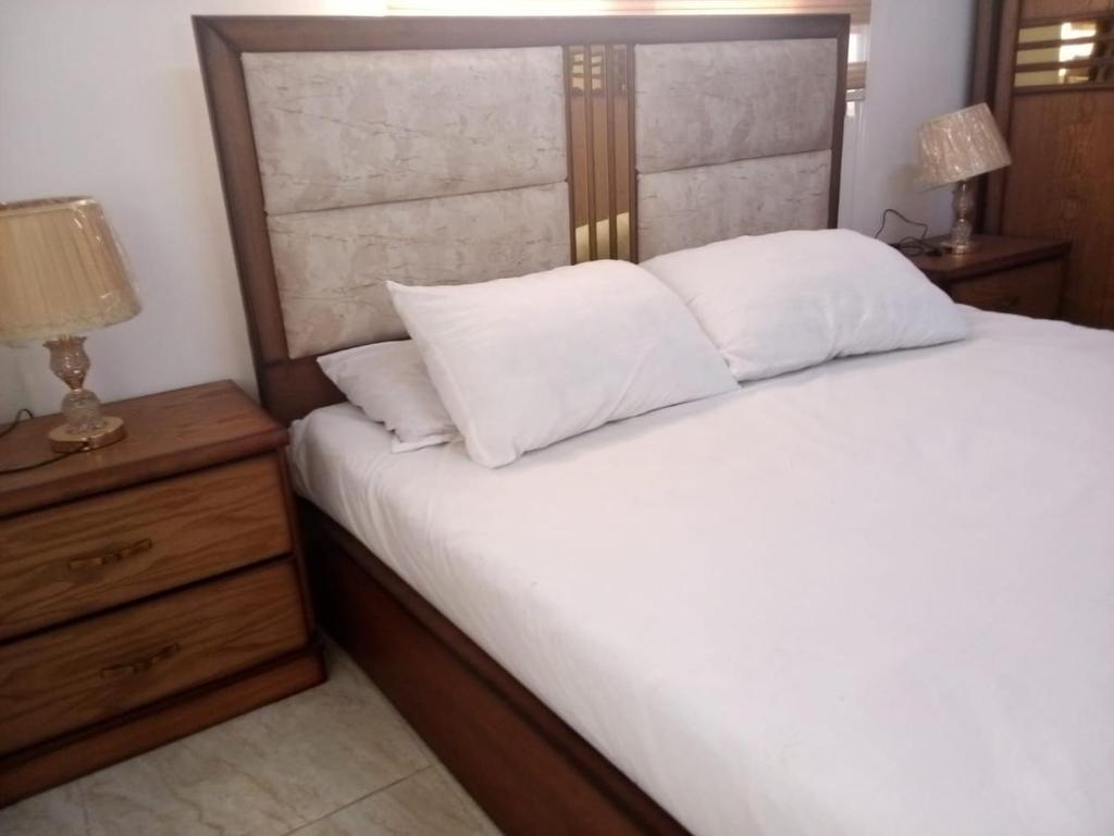 a bedroom with a bed with white sheets and a nightstand at Furnished apartment for rent in jarash شقة مفروشة للإيجار في جرش in Jerash