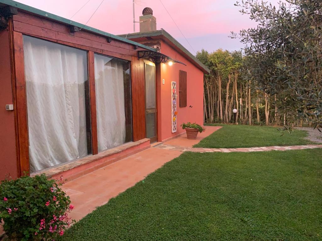 a red house with a patio and a yard at Casa nel verde in Albinia