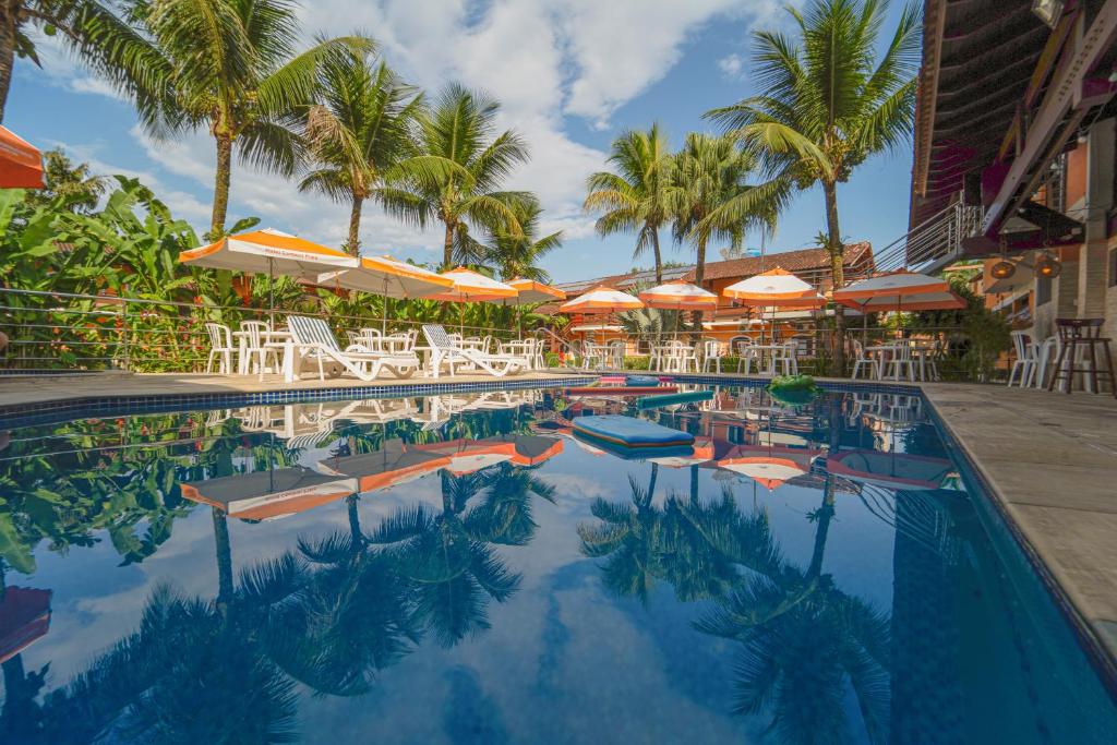 a swimming pool with chairs and umbrellas and palm trees at Hotel Camburi Praia in Camburi