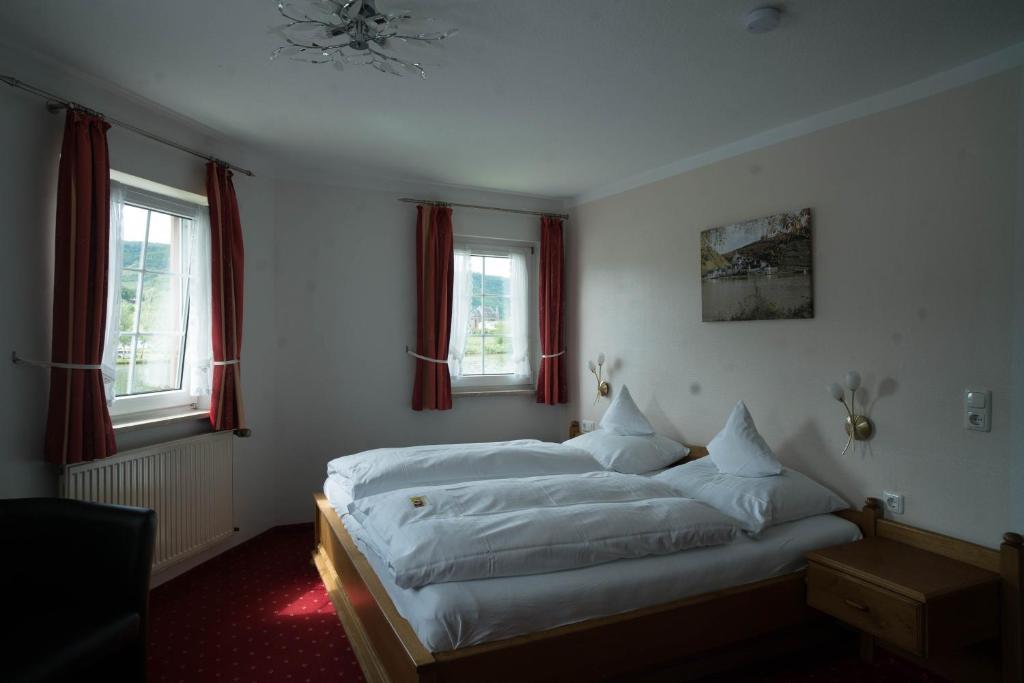 a bedroom with a bed with white sheets and windows at Hotel Haus Burg Metternich in Beilstein