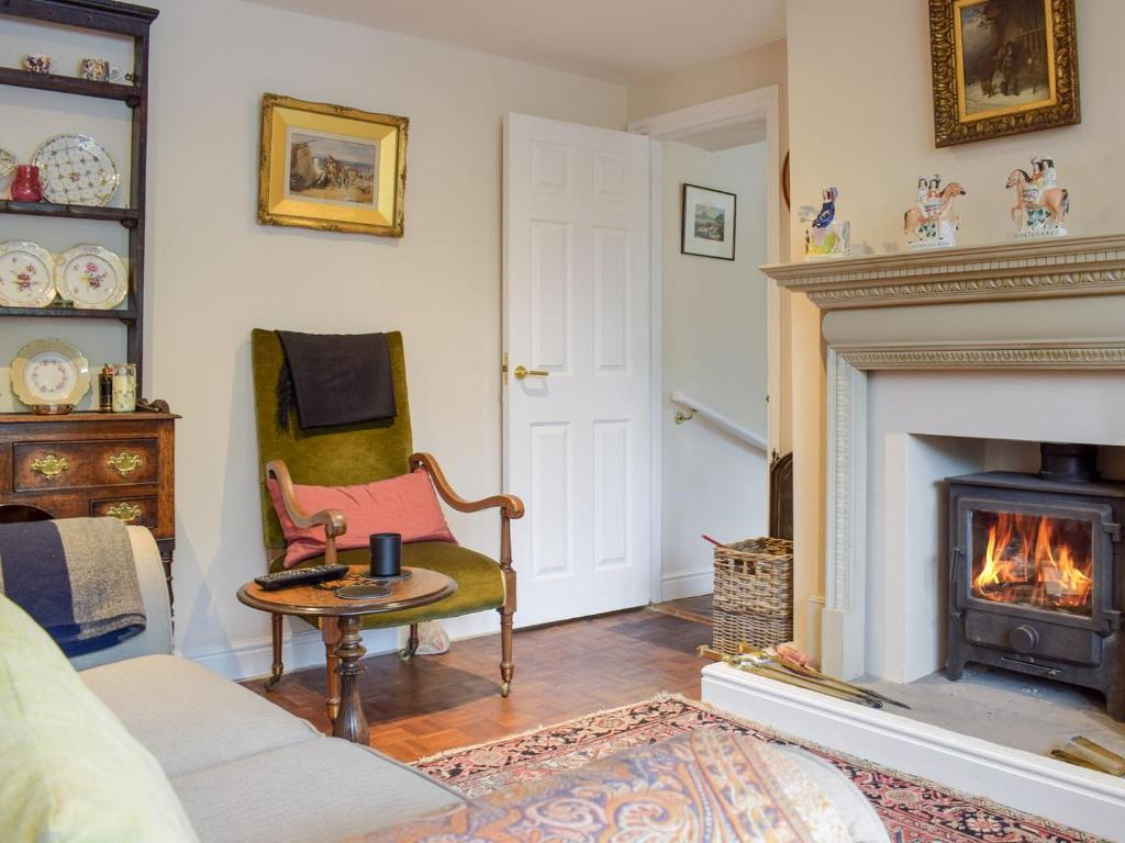 a living room with a fireplace and a chair at Stable Cottage in Much Birch