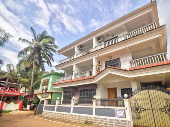 a white building with a balcony and a palm tree at Calangute Beach Corner in Calangute