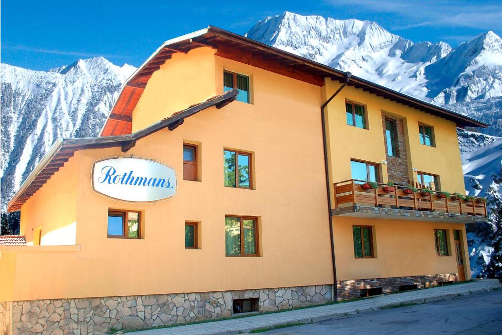 a building with a sign on it in front of mountains at Hotel Rothmans in Bansko
