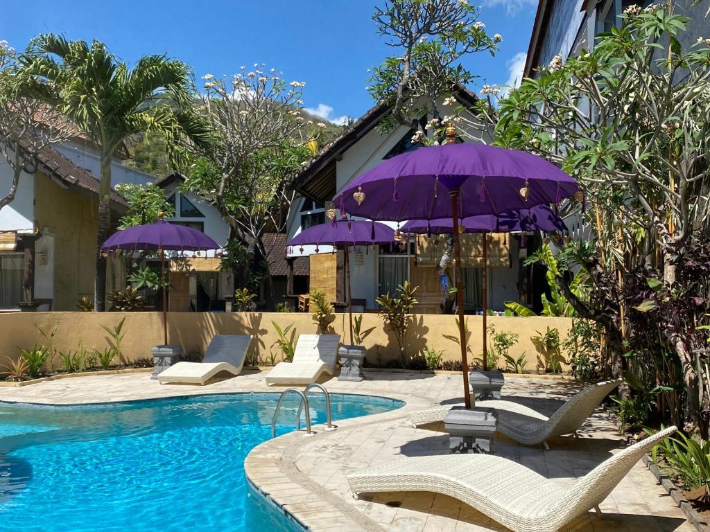 a pool with chairs and purple umbrellas next to a building at Teratai Boutique Resort in Amed