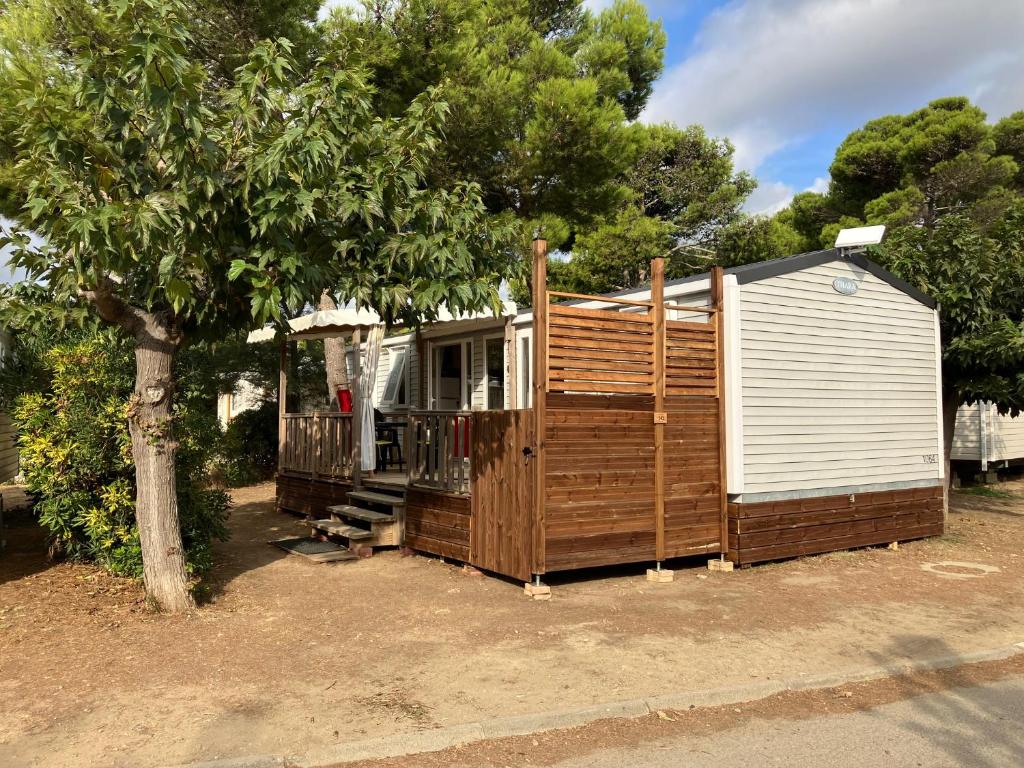 une petite maison assise à côté d'un arbre dans l'établissement Mobil Home - Camping La Falaise, à Narbonne
