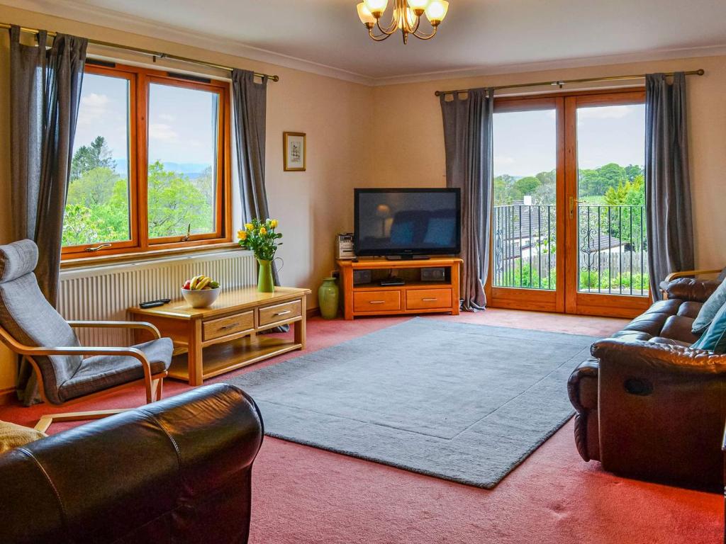 a living room with a couch and a tv and windows at Bramble Cottage in Dalry