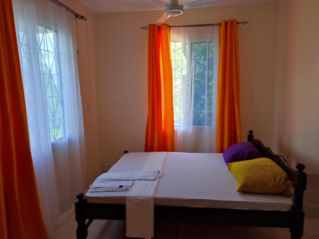 a bed in a room with two windows with curtains at Vee's Villa in Kilifi