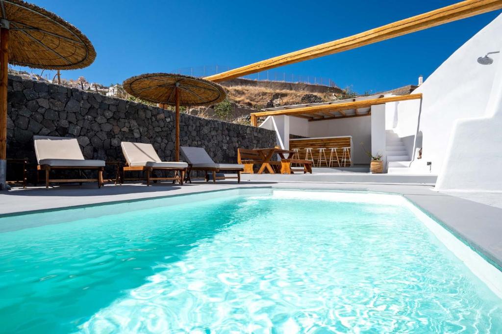 a pool with chairs and umbrellas next to a house at Karpimo Suites in Éxo Goniá