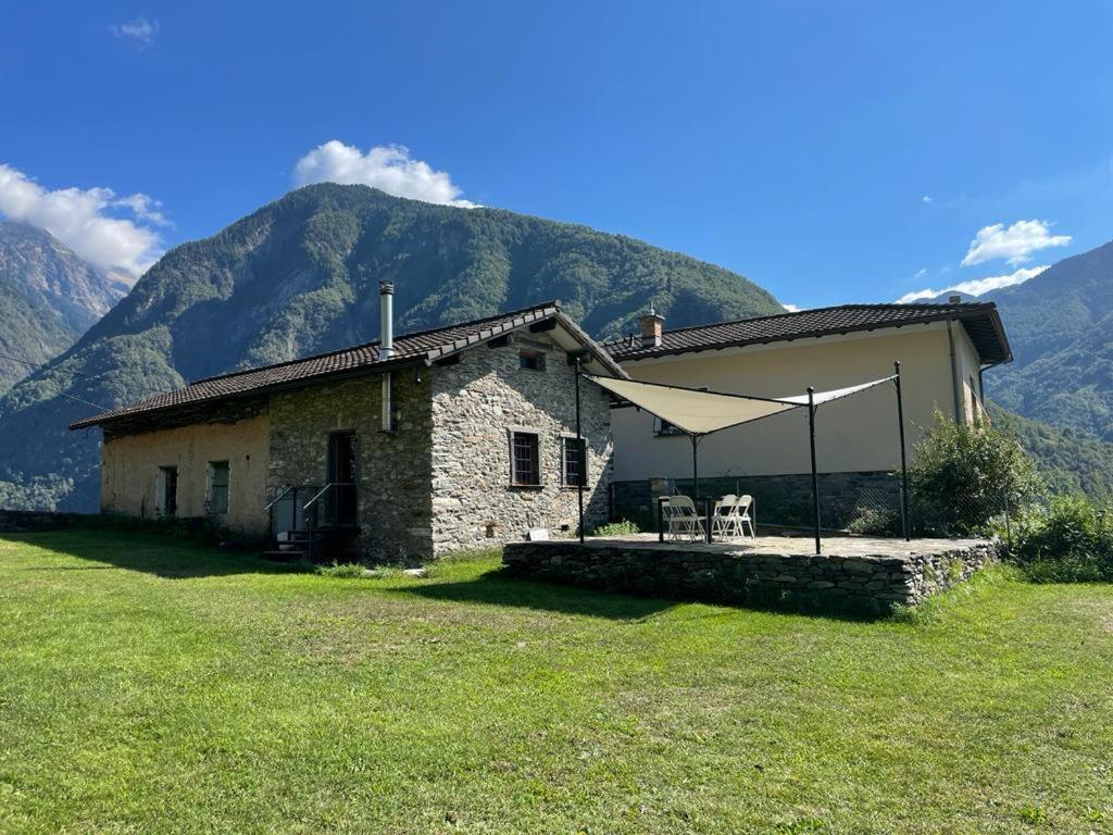 a stone house with a table and chairs in front of mountains at Rustico a Roveredo GR in Roveredo