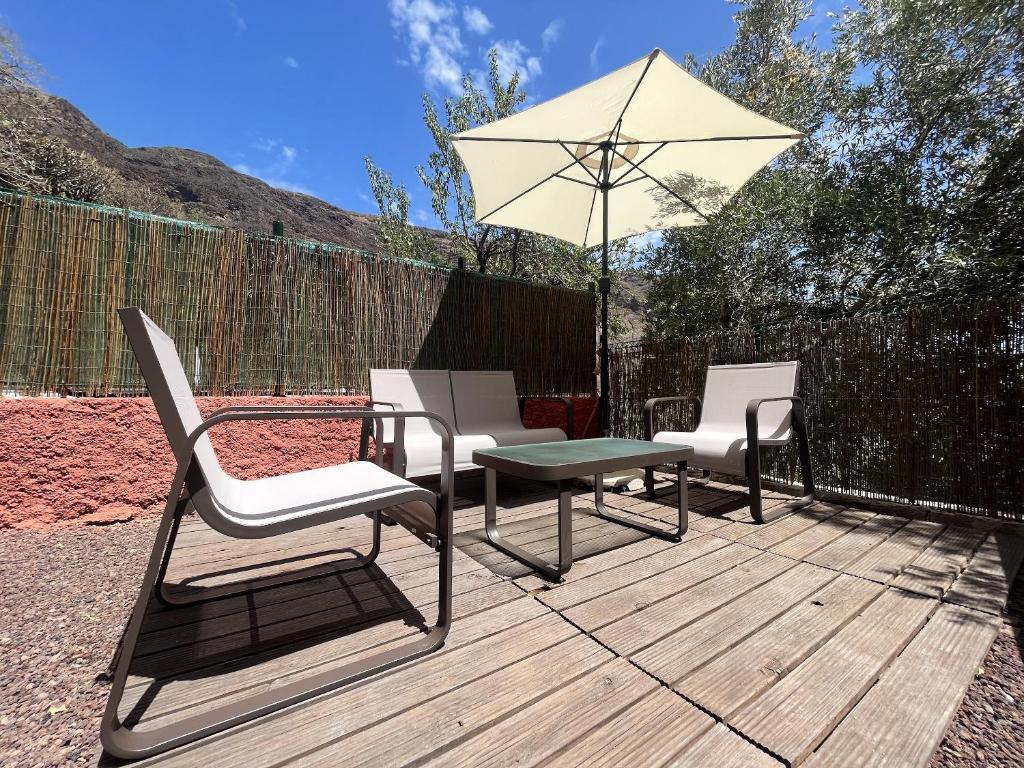 3 Stühle, ein Tisch und ein Regenschirm auf einer Terrasse in der Unterkunft 4 bedrooms house with enclosed garden and wifi at Ingenio in Ingenio