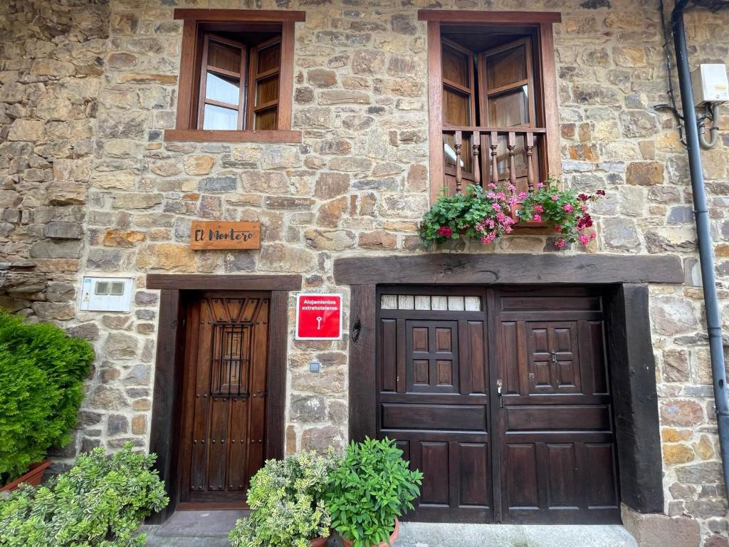 a stone building with two wooden doors and flowers at Casa El Montero in Espinama