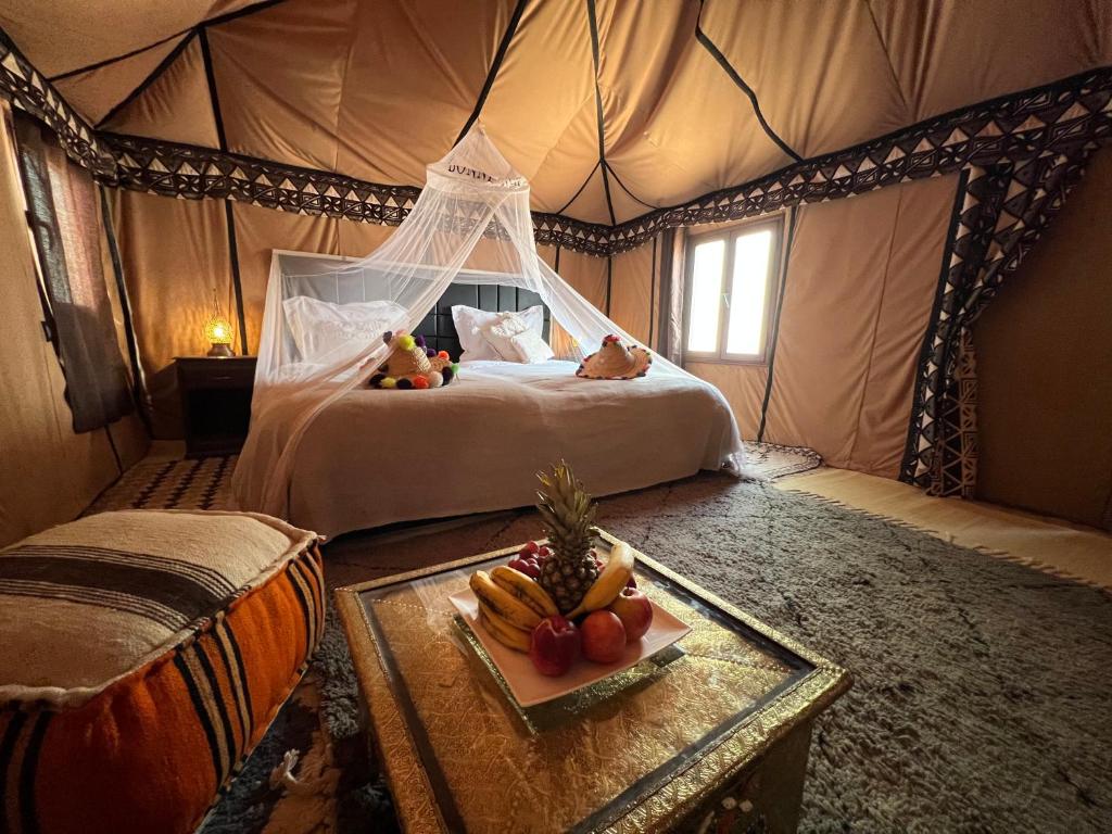 a bedroom with a bed in a tent with a tray of fruit at Luxury traditional Tent Camp in Merzouga