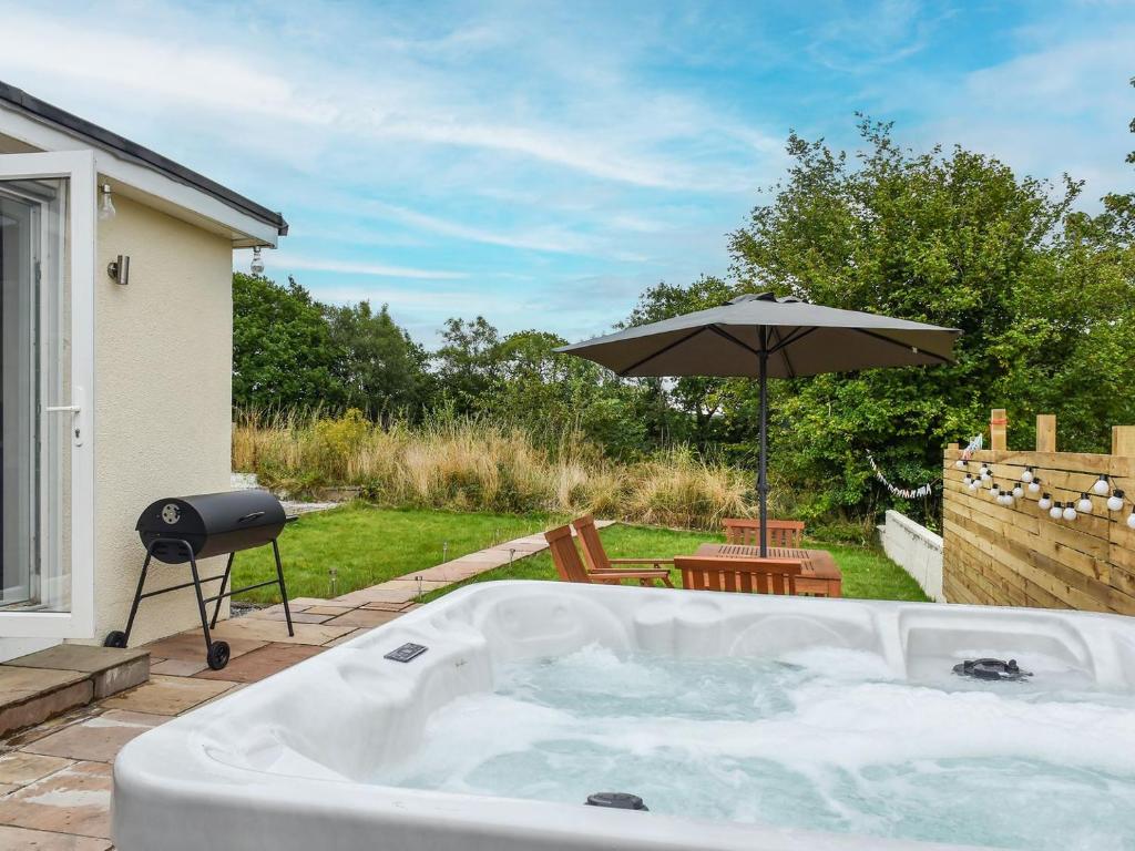 a hot tub in a backyard with an umbrella at Highfield Bungalow in Brynamman