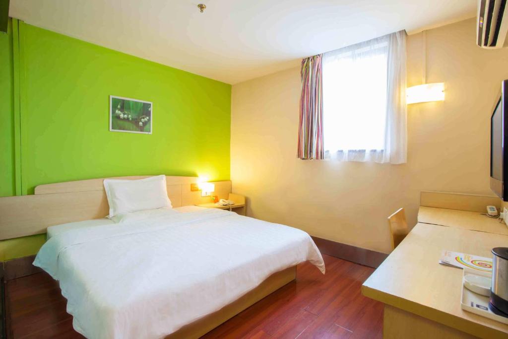 a bedroom with a white bed and a green wall at 7Days Inn Guiyang Huaxi Avenue Zhong Cao Si in Guiyang