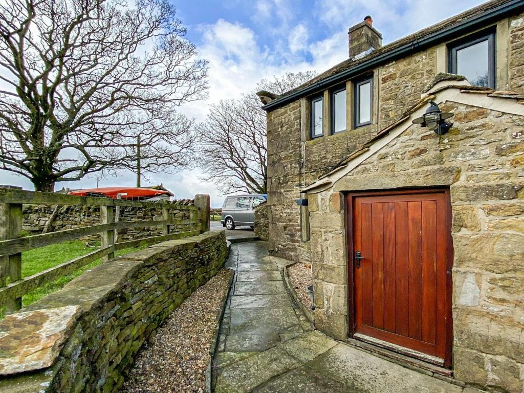 a stone house with a red door and a fence at Cooper Cabana in Elslack