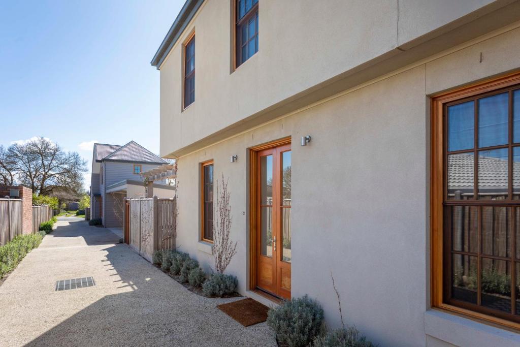 a white house with wooden doors and a sidewalk at Rochville - Luxe, Dog Friendly Townhouse, Kyneton in Kyneton