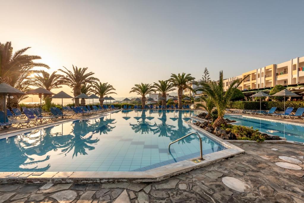 a large swimming pool with palm trees and a hotel at Mediterraneo Hotel in Hersonissos