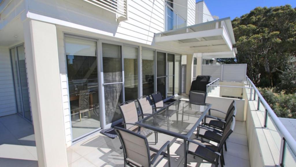 a balcony with a glass table and chairs on a house at 8 - 22 Bennett St, Hawks Nest in Hawks Nest