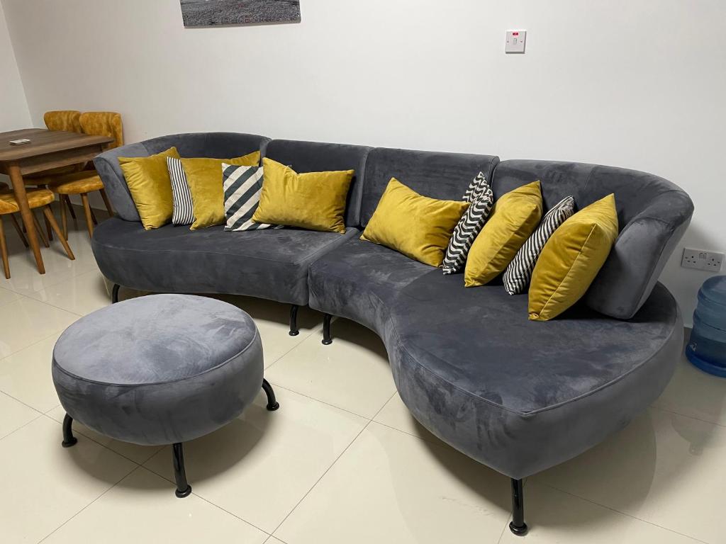 a grey couch with yellow pillows and a stool at Girne Merkez Cozy 2+1 Daire wifi +netflix in Kyrenia