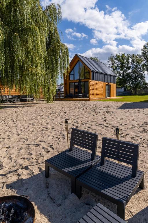 two benches sitting in the sand in front of a house at Domki Kunice in Kunice