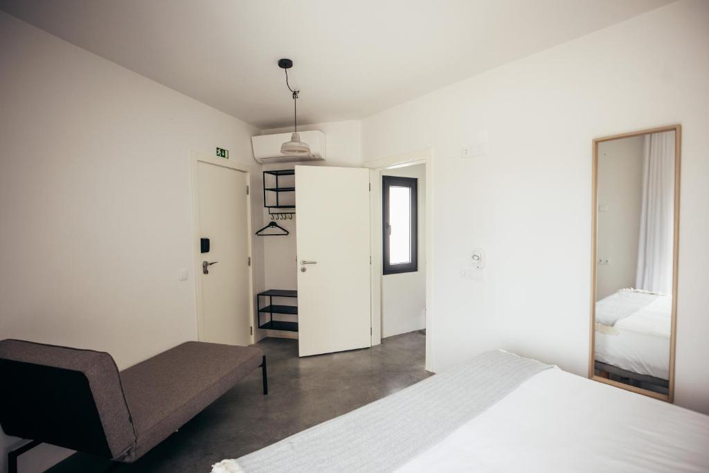 a white bedroom with a bed and a chair at MUTE Hostel Porto Covo in Porto Covo