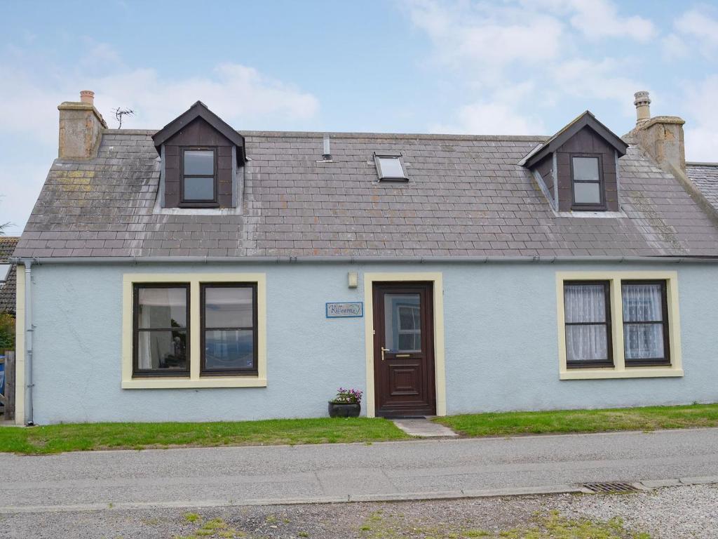 a white house with a brown door on a street at Killearn Cottage in Portmahomack