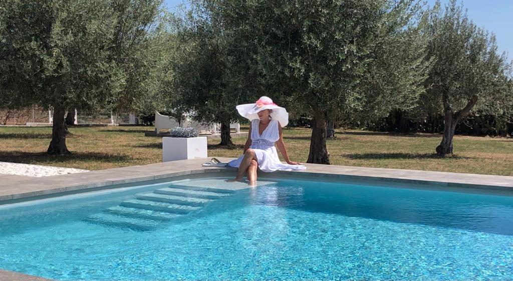a woman with an umbrella sitting next to a swimming pool at Villa private Siracusa luxury in Augusta