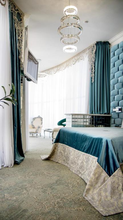 a bedroom with a bed with blue curtains and a chandelier at Boutique Spa Casino Hotel Lybid Plaza in Khmelnytskyi