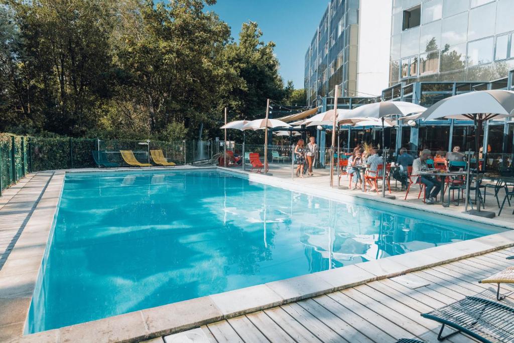 a blue swimming pool with people sitting at tables and umbrellas at Novotel La Rochelle Centre in La Rochelle
