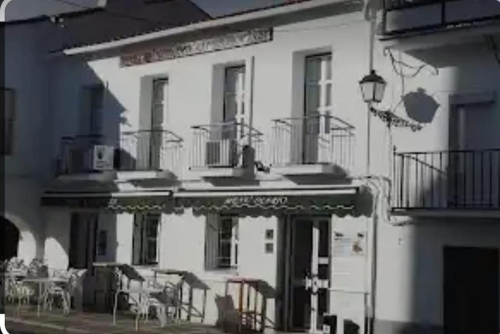 um edifício branco com mesas e cadeiras em frente em Hostal 2 estrellas -Restaurante Las Tres Encinas em Cabeza la Vaca
