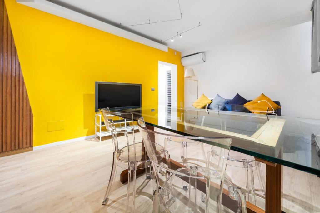 a living room with a yellow wall and a glass table at Maison Giulia ai Giardini in Bologna
