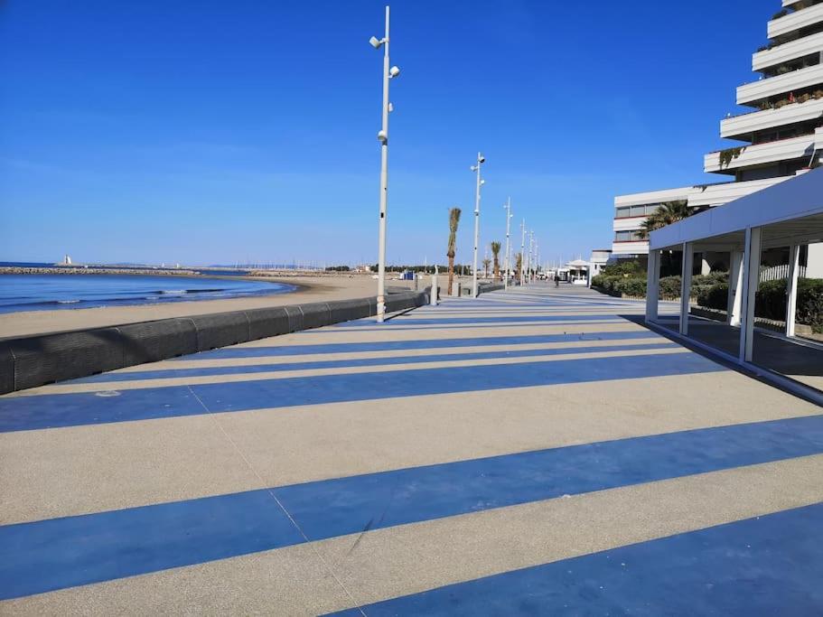 a sidewalk next to a beach with a building at Résidence arc en ciel, proche de la plage accés direct ,internet et parking privatif gratuit in La Grande Motte