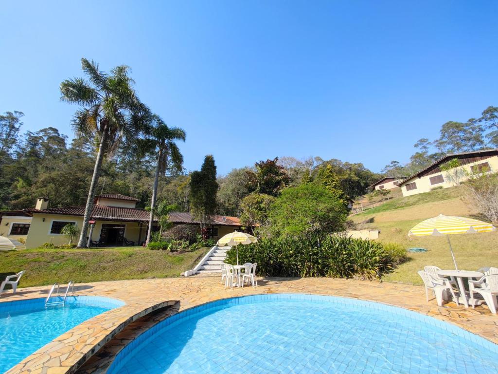 una piscina con sillas y sombrillas junto a una casa en Pousada Green Valley, en São Roque