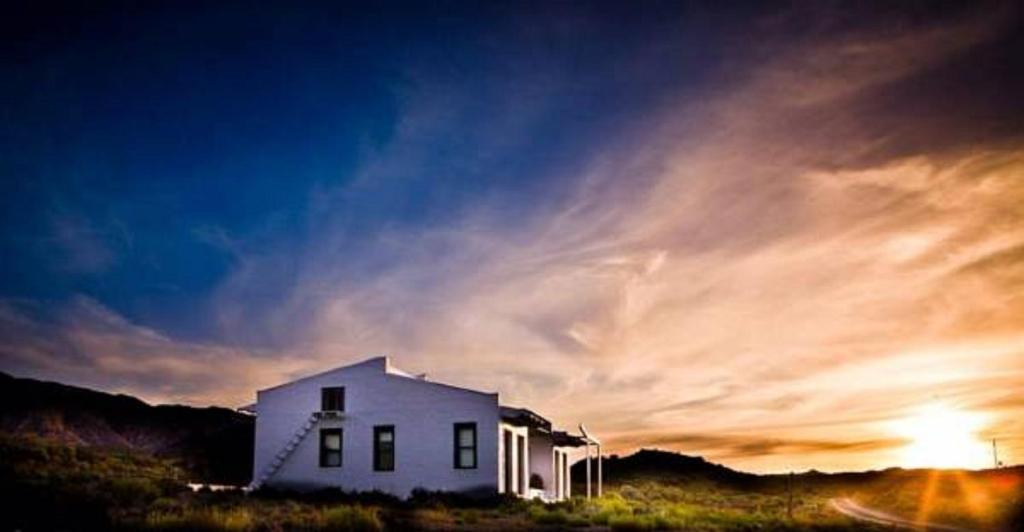a white house in a field with a sunset at Vrisch Gewagt Boutique Self-Catering Olive Farm in Prince Albert