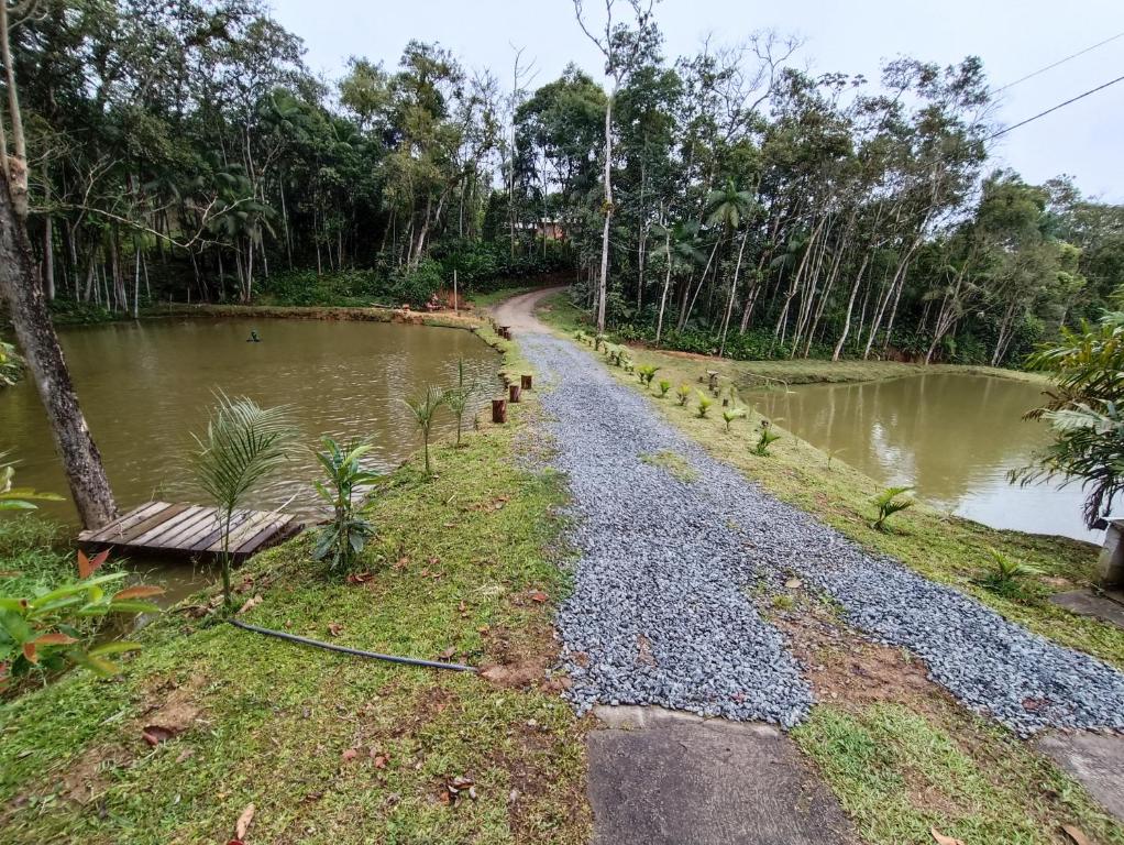 a gravel road next to a river with a bench at Chácara Aconchego in Blumenau