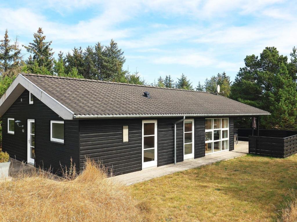 une maison noire avec une terrasse couverte et une cour dans l'établissement Three-Bedroom Holiday home in Ålbæk 21, à Ålbæk