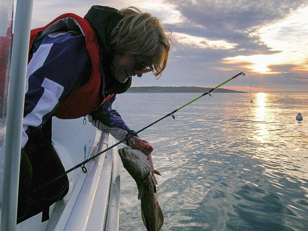 una persona sosteniendo un pez en un barco en Holiday home Selsøyvik, en Håkaringen