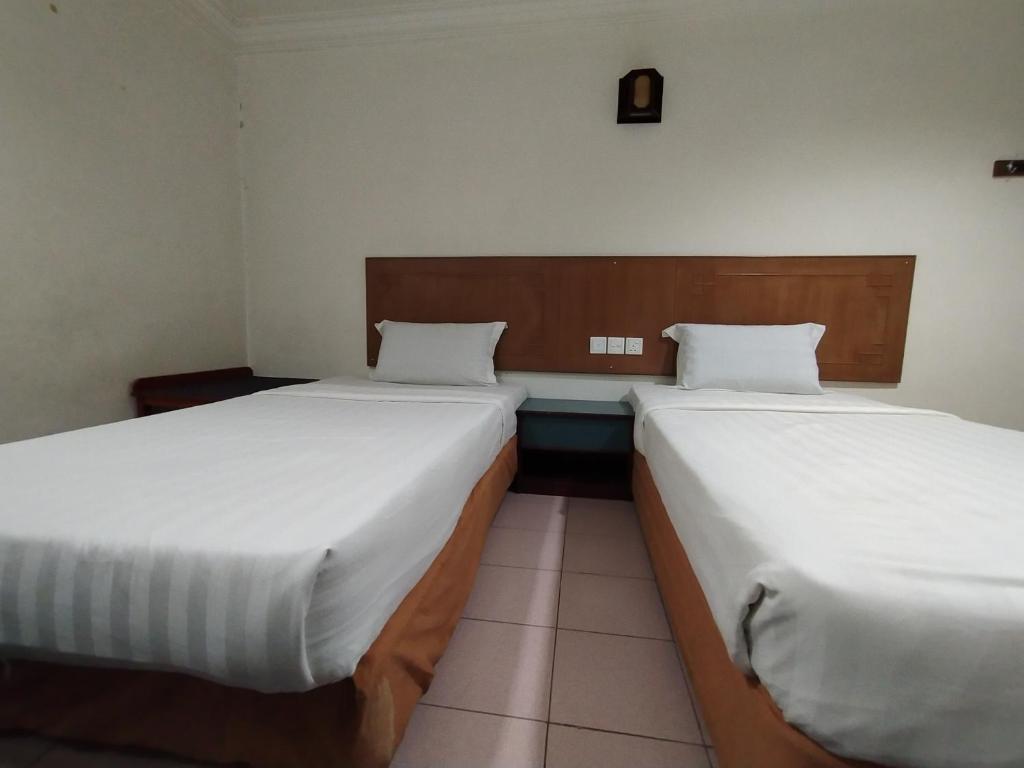 two beds in a hotel room with white sheets at Faber Inn in Bintulu